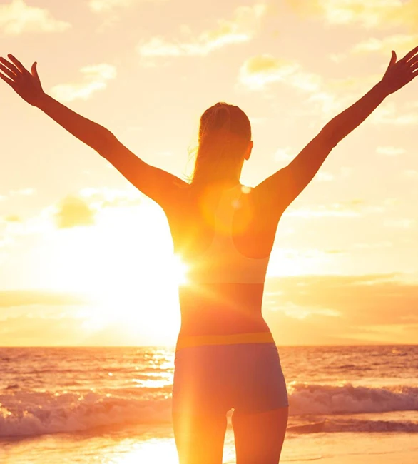 Longevity and wellness compounding: person with arms raised at a beach sunrise