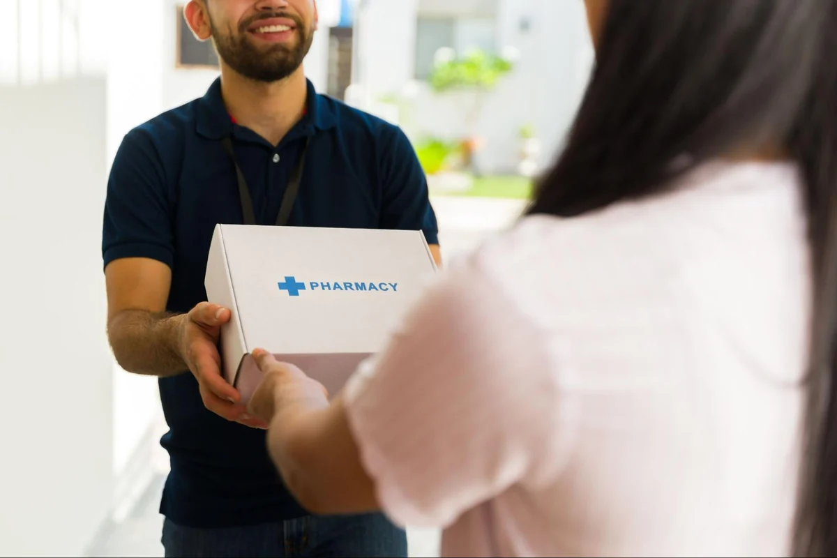 Pharmacy courier handing a boxed medication delivery to a patient at her front door
