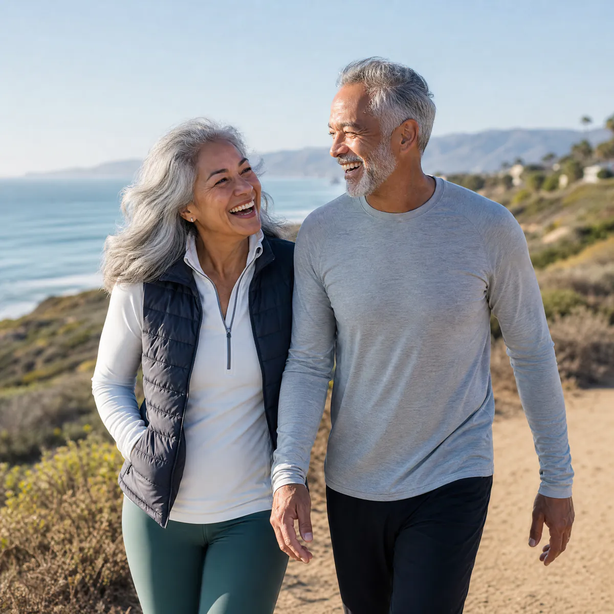 Active couple in their sixties hiking a sunny coastal trail, illustrating our wellness compounding pharmacy