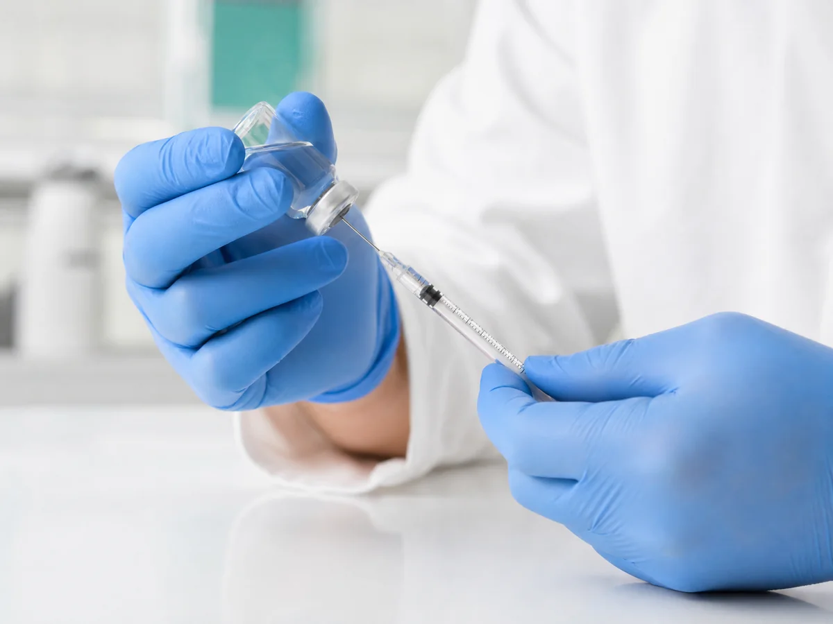 Gloved hands drawing medication from a vial into a syringe