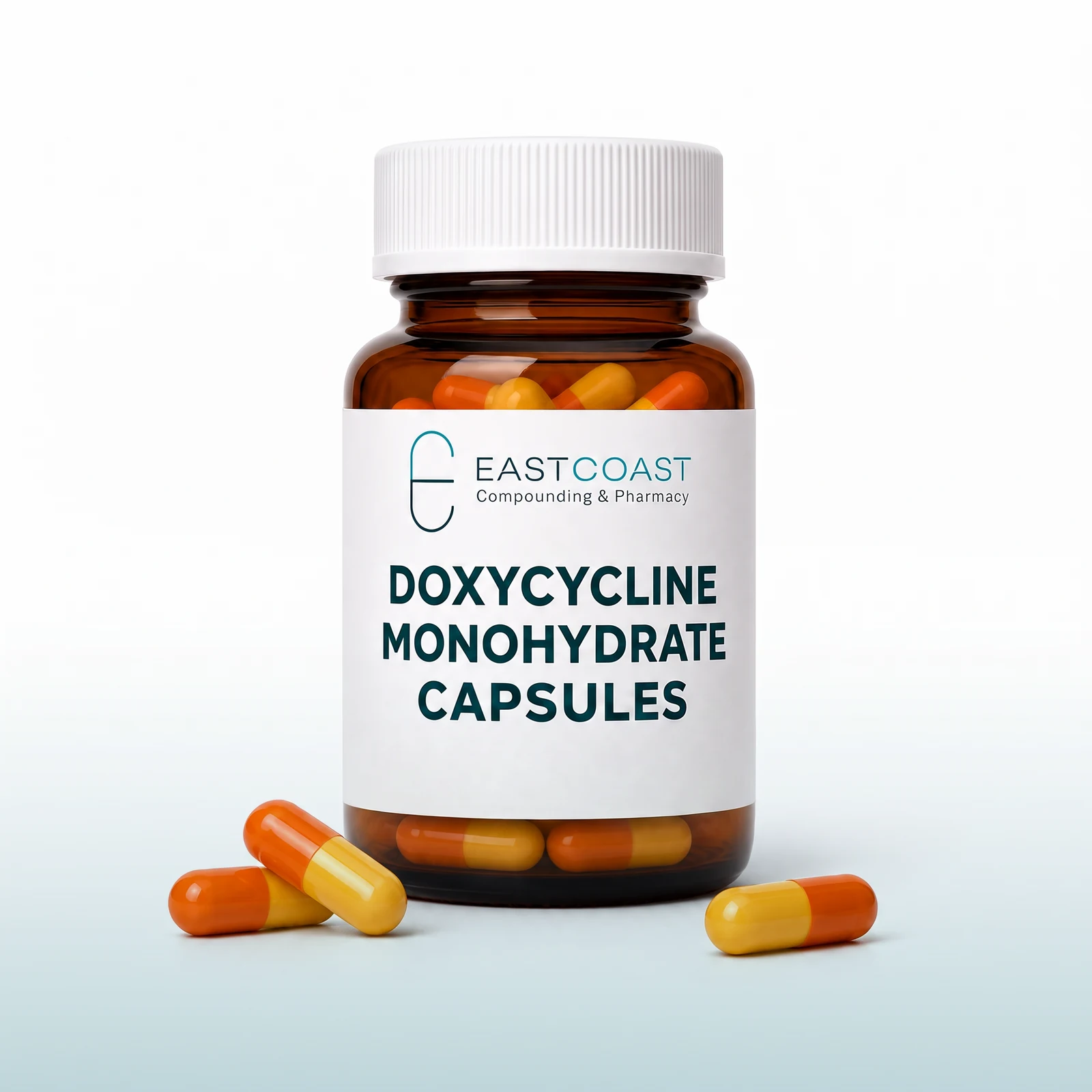 Doxycycline monohydrate capsules in an amber pharmacy vial with East Coast Compounding & Pharmacy label, yellow-orange capsules beside it (illustrative image)