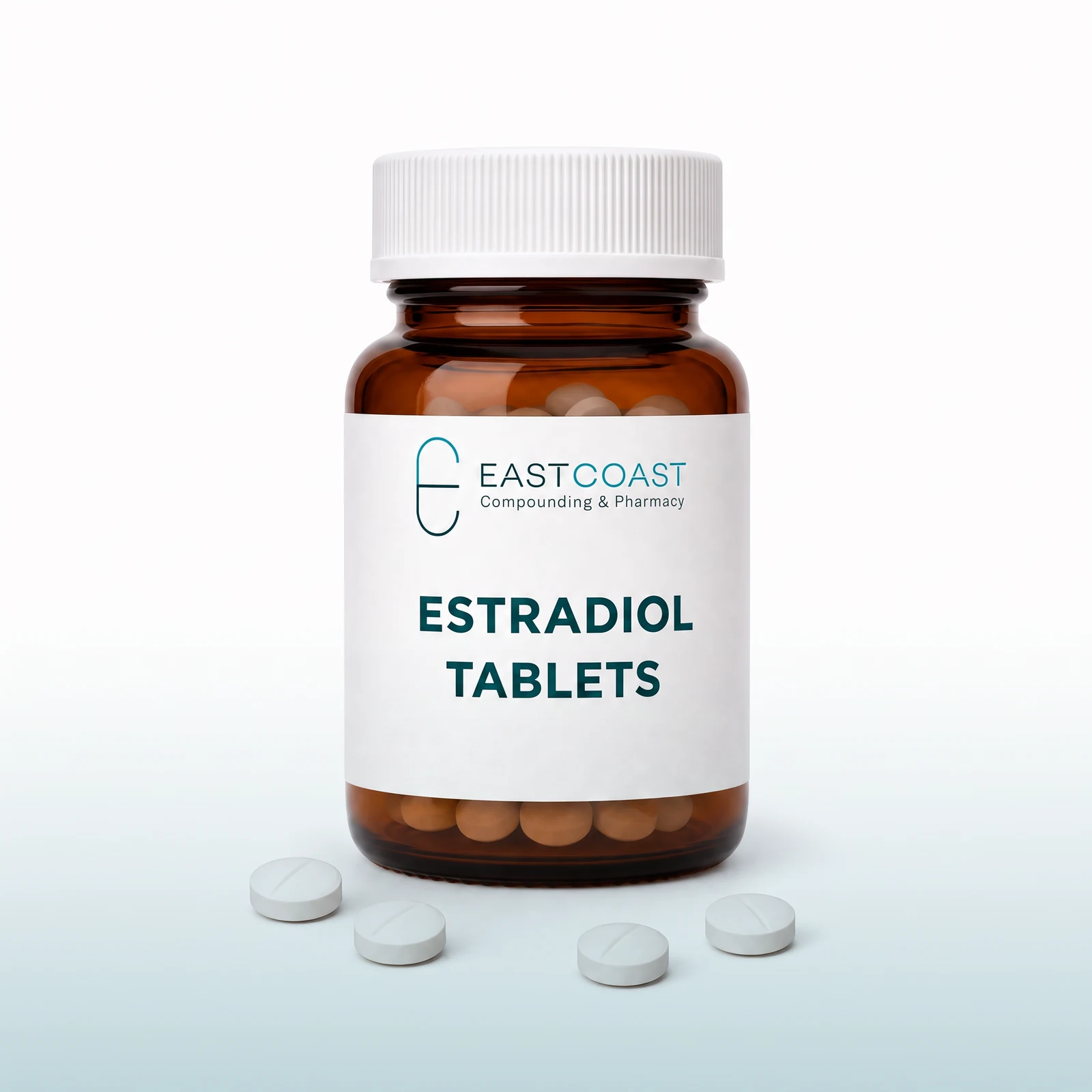 Estradiol tablets in an amber pharmacy vial with East Coast Compounding & Pharmacy label, white tablets beside it (illustrative image)
